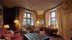 A traditional room with a red sofa, multiple chairs, a leather ottoman, and two windows with curtains. - The Hunting Tower Chatsworth Estate (Chatsworth)