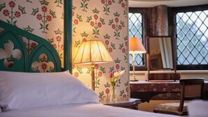 A hotel room with floral wallpaper, a bed with white linens, a green headboard, a bedside table with a lamp, a vase with flowers, and a window with a view. - The Hunting Tower Chatsworth Estate (Chatsworth)