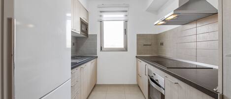 A narrow kitchen with white cabinets, a stainless steel range hood, and a window above the sink.