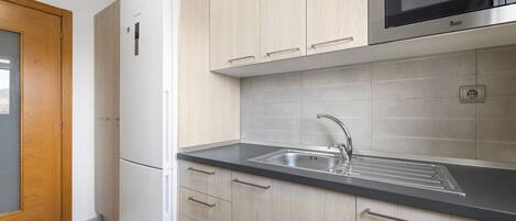 A modern kitchen with light wood cabinets, a stainless steel sink, and a built-in microwave.
