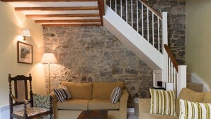 Ein Wohnzimmer mit Steinwand, Holzbalken, einer Couch, einem Sessel und einer Treppe.