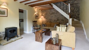 Ein gemütliches Wohnzimmer mit Steinwand, Holzbalken, einer Couch, einem Couchtisch, einem Kamin und einer Treppe.