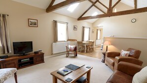 A living room with a wooden table, leather sofa, and a television on a wooden cabinet. - Heron Cottage, Upperdale | Peak District (Buxton)