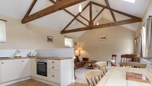 A spacious kitchen with wooden beams, a dining area with a large wooden table, and a cozy seating area with a sofa and chairs. - Heron Cottage, Upperdale | Peak District (Buxton)