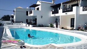 Una piscina con una persona en el agua, rodeada de edificios blancos modernos con balcones y un suelo de baldosas con diseño.