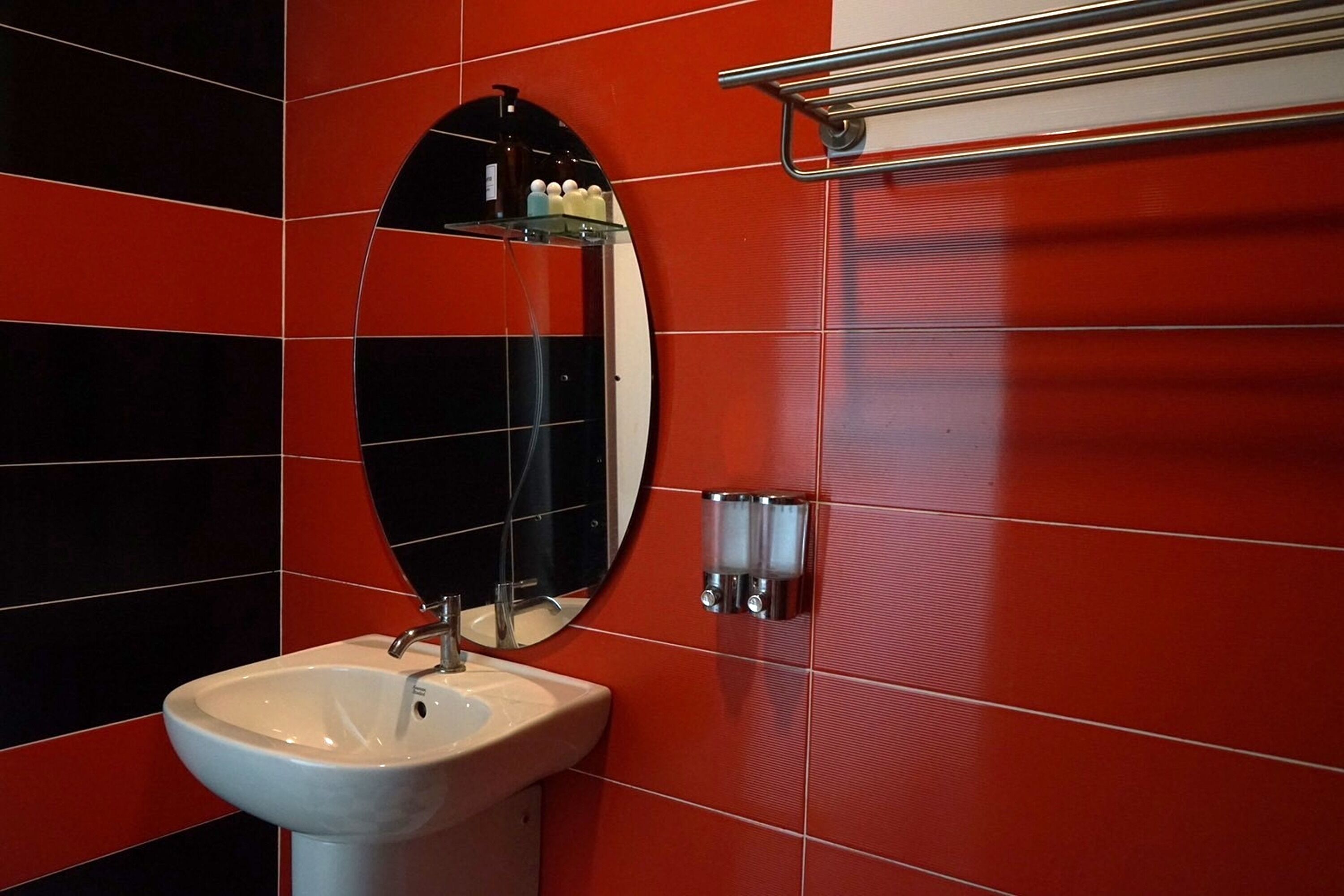 A bathroom with a white sink, a mirror, and red and black tiled walls.