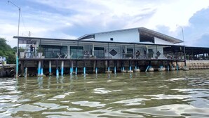 Un edificio moderno con techo plano y ventanas grandes, elevado sobre el agua sobre pilares.