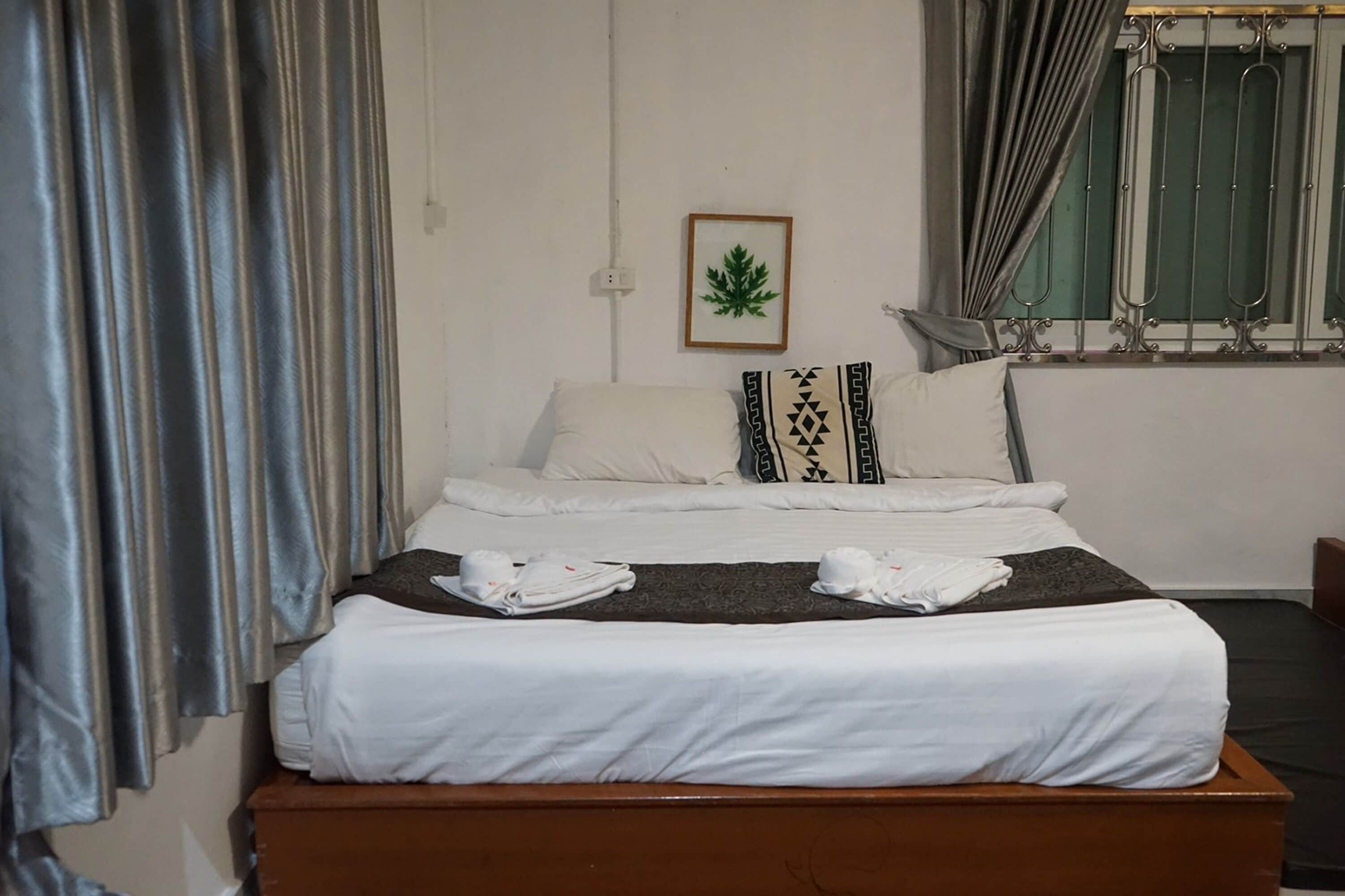 A neatly made bed with white linens and a decorative pillow. A framed picture hangs on the wall above the bed.