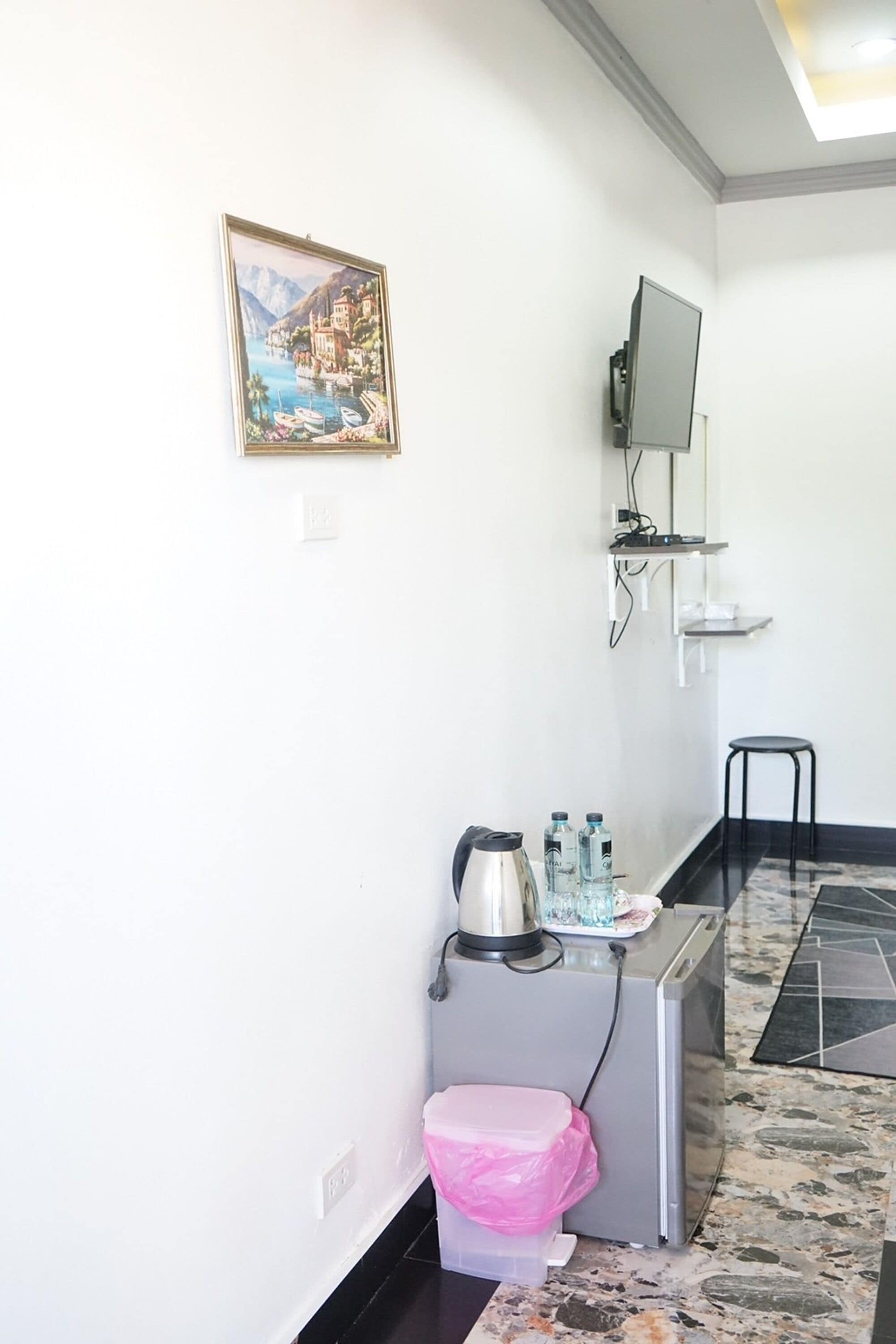 A small kitchenette with a coffee maker, water bottles, and a pink trash bin.