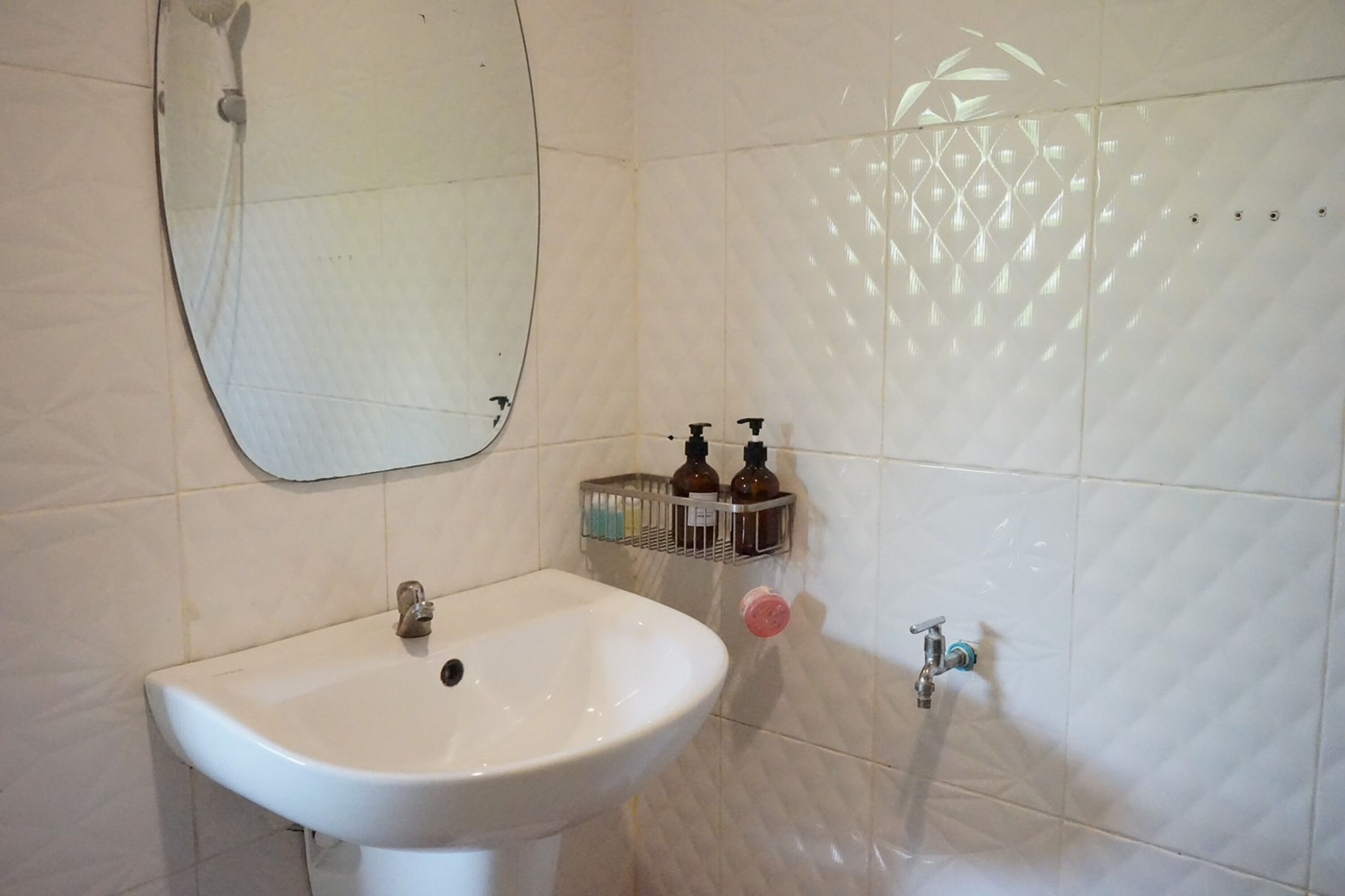 A bathroom with a white sink, a mirror, a shower, and a tiled wall with a geometric pattern.