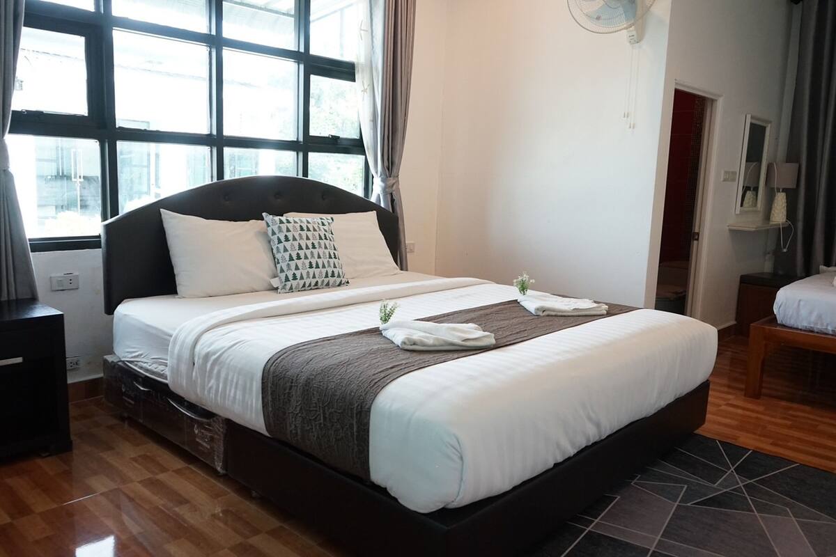 A neatly made bed with white and gray bedding, a dark headboard, and a window with curtains.