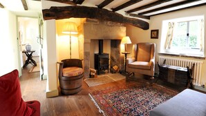 A cozy room with exposed wooden beams, a stone fireplace, a comfortable armchair, and a patterned rug.