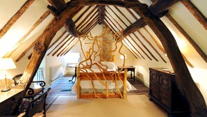 A bedroom with a sloped ceiling, wooden beams, a bed with a wooden frame, a dresser, and a lamp on a bedside table.