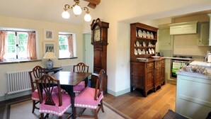 A dining area with a wooden table and chairs, a large clock, and a cabinet with dishes.