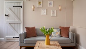 A living room with a grey sofa, a yellow vase with flowers, and framed botanical prints on the wall. - Stable Cottage Chatsworth Estate (Baslow)