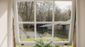 A window with a view of a backyard, a stone building, and a wooden fence. - Stable Cottage Chatsworth Estate (Baslow)