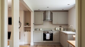 A modern kitchen with grey cabinets, a built-in oven, and a wooden dining table. - Stable Cottage Chatsworth Estate (Baslow)