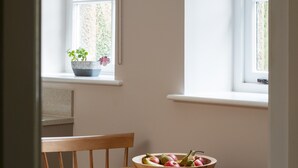 A dining area with a wooden table, chairs, a bowl of fruit, and a hanging light fixture. - Stable Cottage Chatsworth Estate (Baslow)