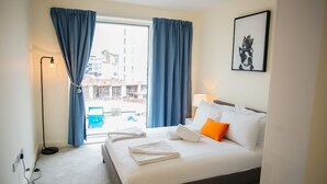 A hotel room with a bed, a window with curtains, a lamp, and a framed picture on the wall. - Thames View 2 Bed Apartment With Balcony (London)