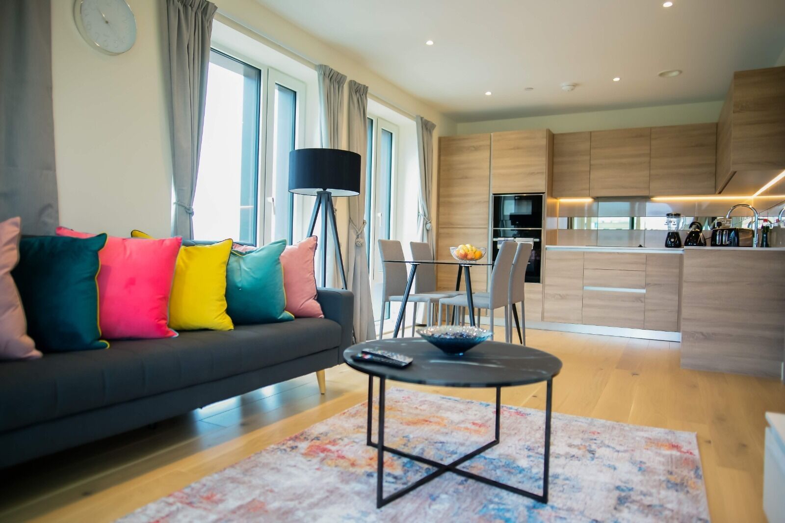 Uma sala de estar moderna com sofá, almofadas coloridas, mesa de centro e área de jantar com cadeiras.