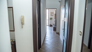 Um corredor com um telefone, um vaso de planta e uma porta que dá para outro quarto.