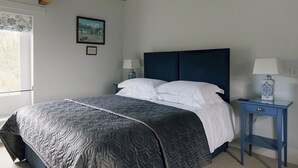 Une chambre à coucher avec un lit, deux tables de chevet avec des lampes, une fenêtre et un tableau encadré au mur.