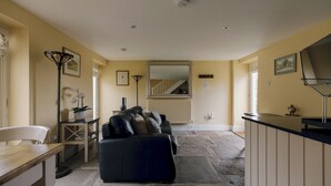 Un salon avec un canapé foncé, une table en bois, un lampadaire et un escalier menant à un niveau supérieur.