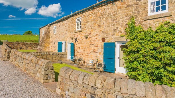 A stone building with two doors, a small patio with chairs, and a stone wall. - Rowsley Cottage, Bakewell | Peak District (Bakewell)