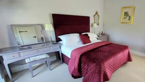 A bedroom with a large bed, a vanity with a mirror, and a nightstand with a lamp. - Rowsley Cottage, Bakewell | Peak District (Bakewell)