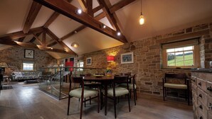 A rustic dining area with a stone wall, wooden beams, and a view of the countryside. - Rye Croft Cottage on the Chatsworth Estate (Edensor)