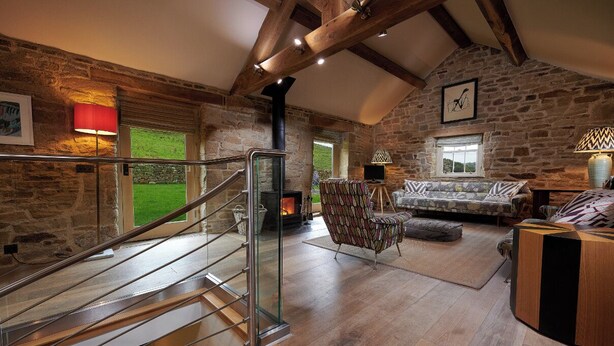 A rustic interior with a stone wall, a wooden staircase, a sofa, and a fireplace. - Rye Croft Cottage on the Chatsworth Estate (Edensor)