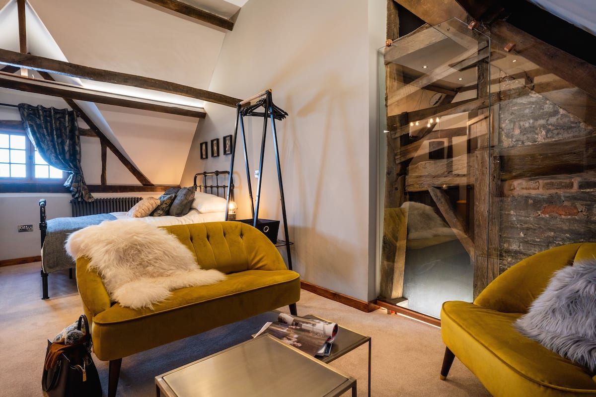 A modern loft bedroom with a bed, a sofa, and a glass-walled fireplace.