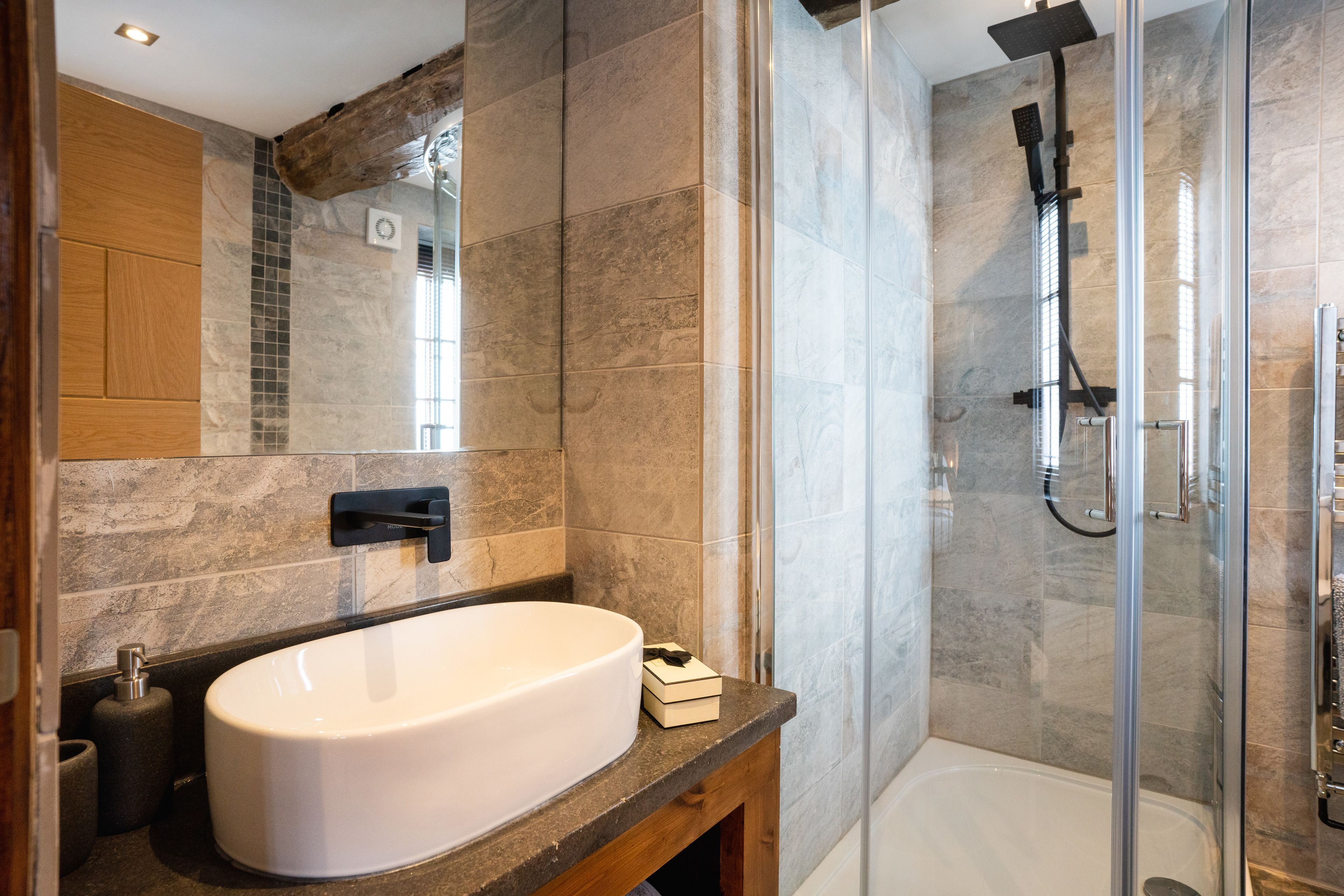 A modern bathroom with a large white sink, a glass-enclosed shower, and a wooden vanity.