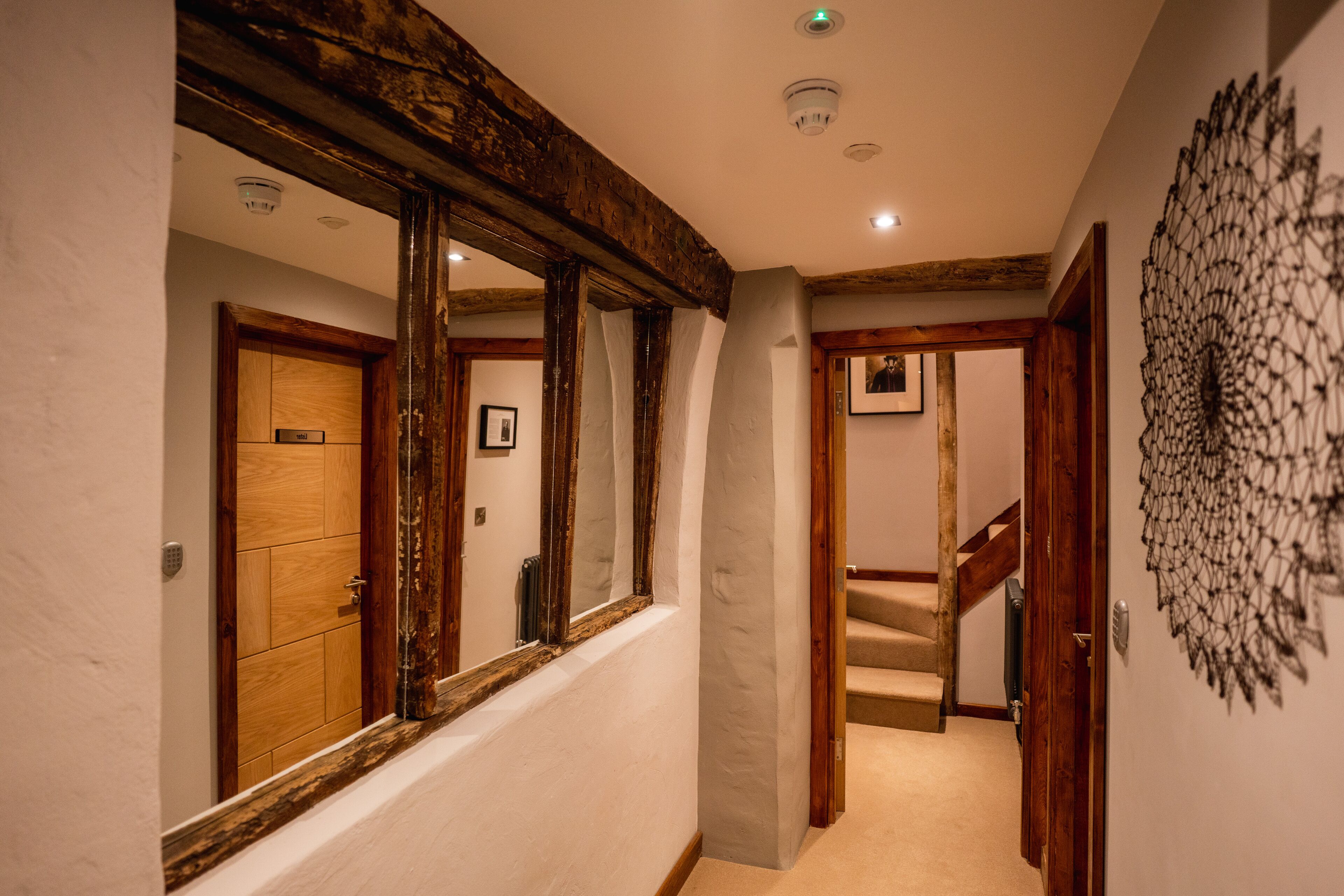 Un couloir avec des poutres en bois, un miroir, une porte et un escalier.