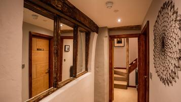 Un pasillo con vigas de madera, un espejo, una puerta y una escalera.