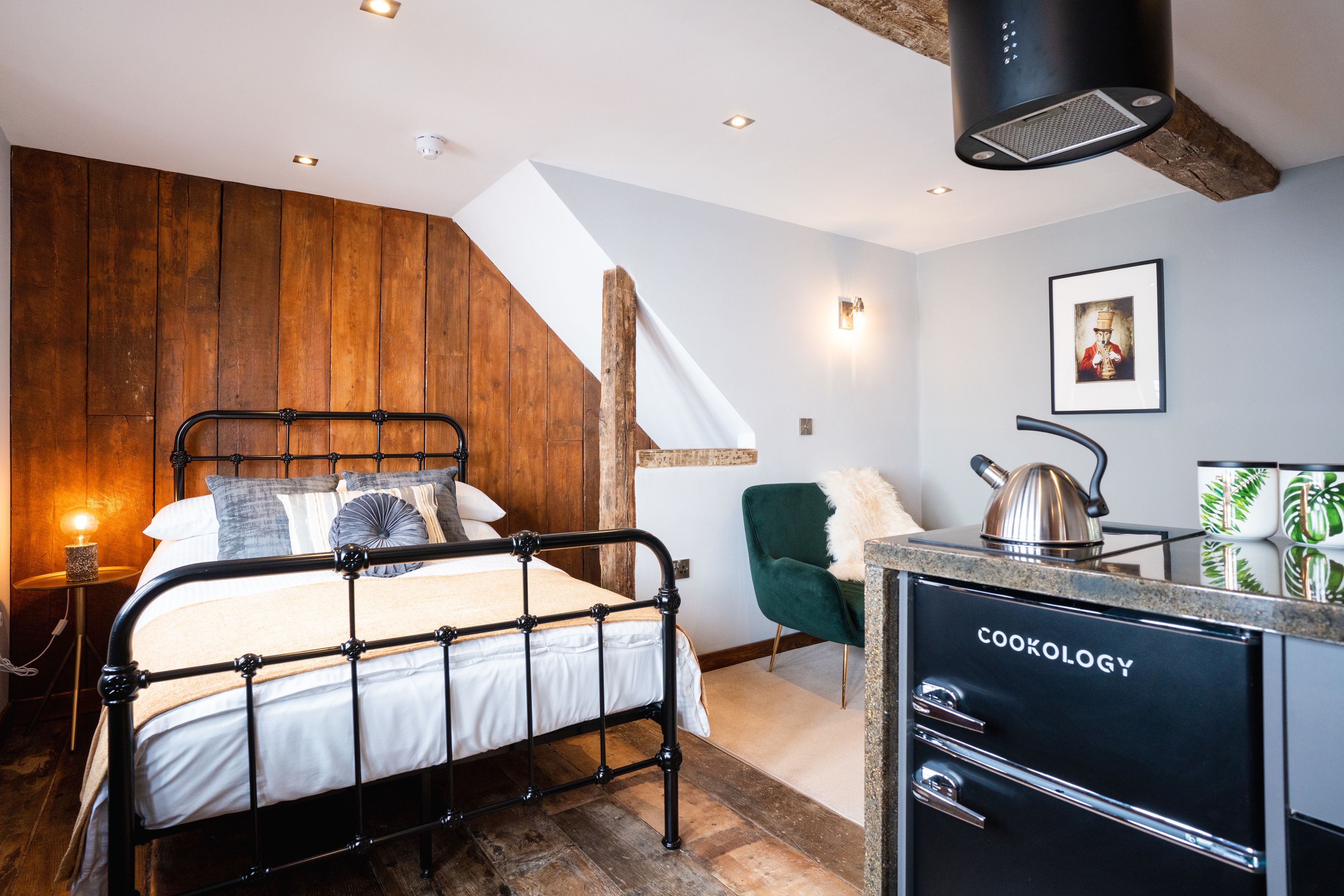 Ein Schlafzimmer mit einem Bett, einer Holzwand, einem grünen Stuhl, einer Küchenzeile und einer Treppe.