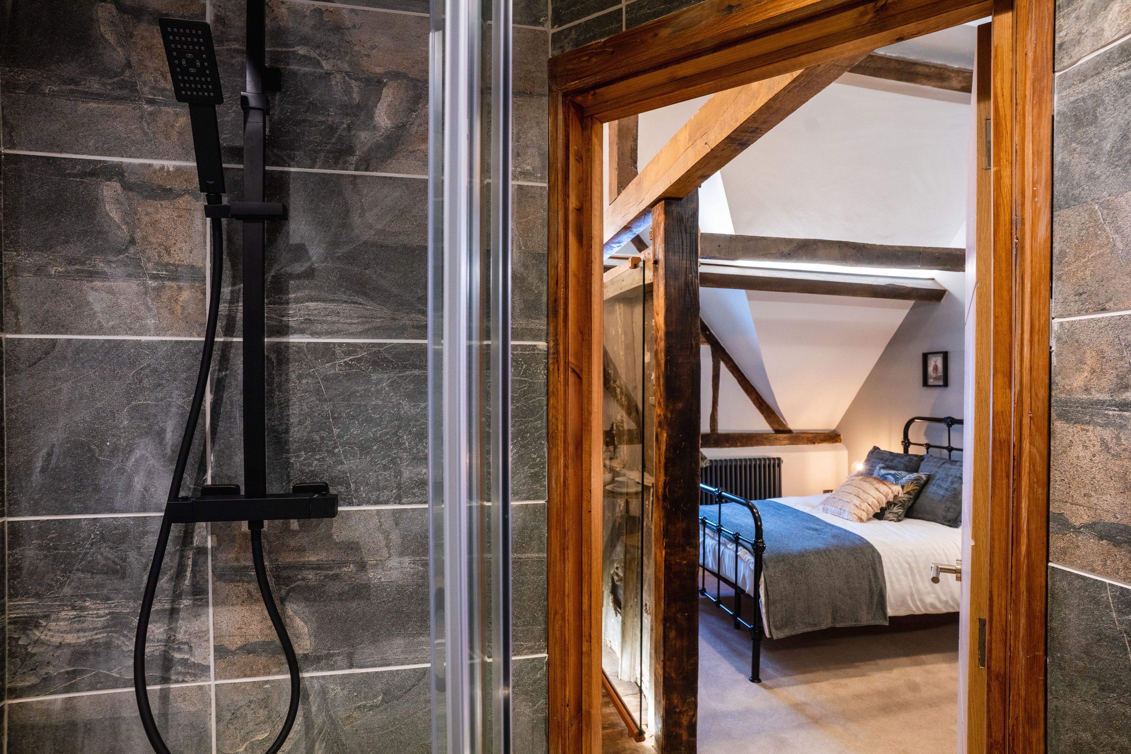 A modern bathroom with a shower, stone walls, and a wooden ceiling beam.
