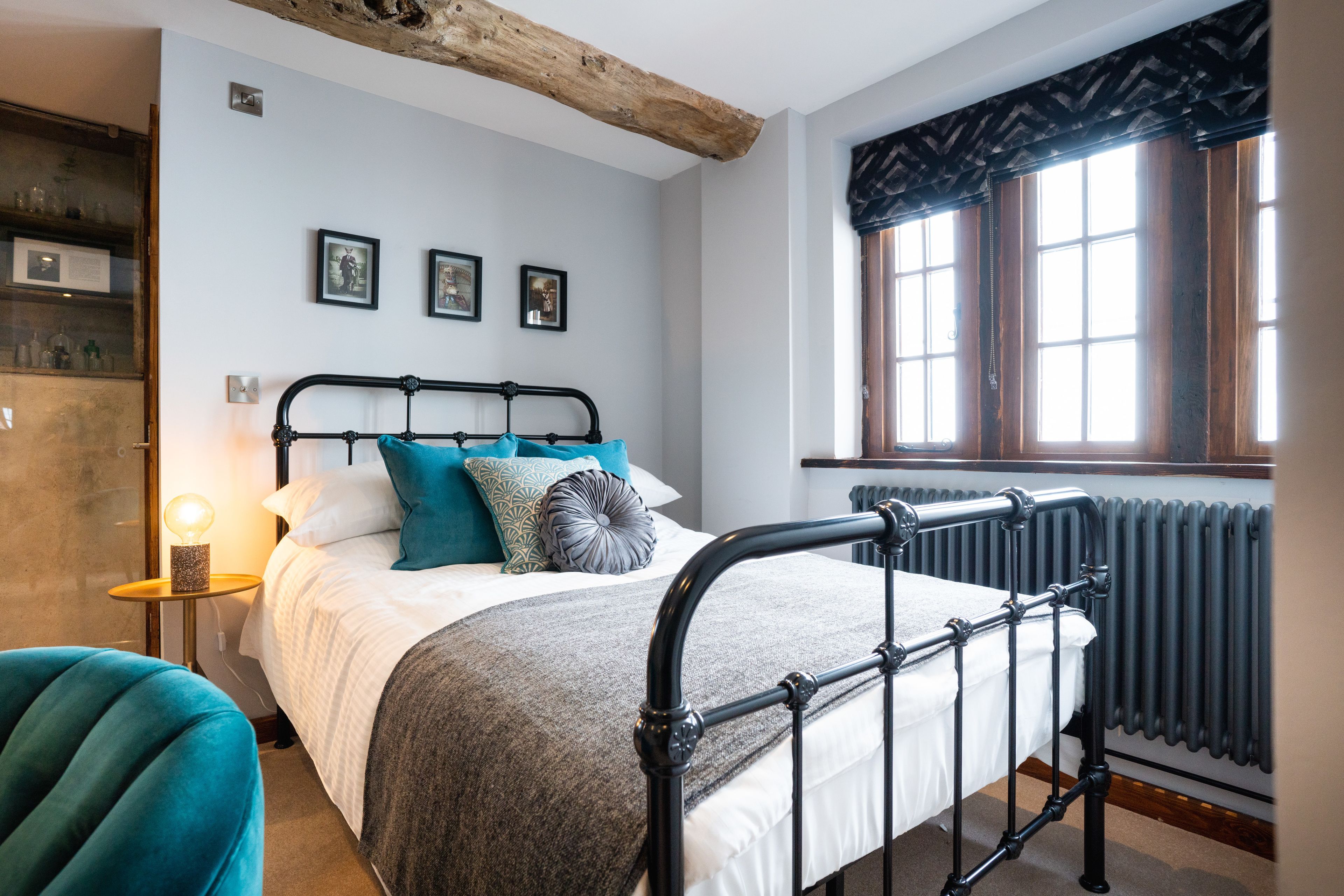 A bedroom with a bed, a nightstand, a lamp, a window with curtains, and a radiator.
