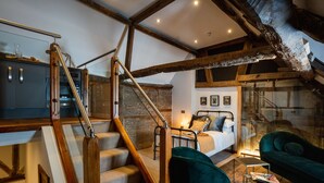 Amplio dormitorio tipo loft con una cama grande, un sillón verde y una escalera que sube a un nivel superior.