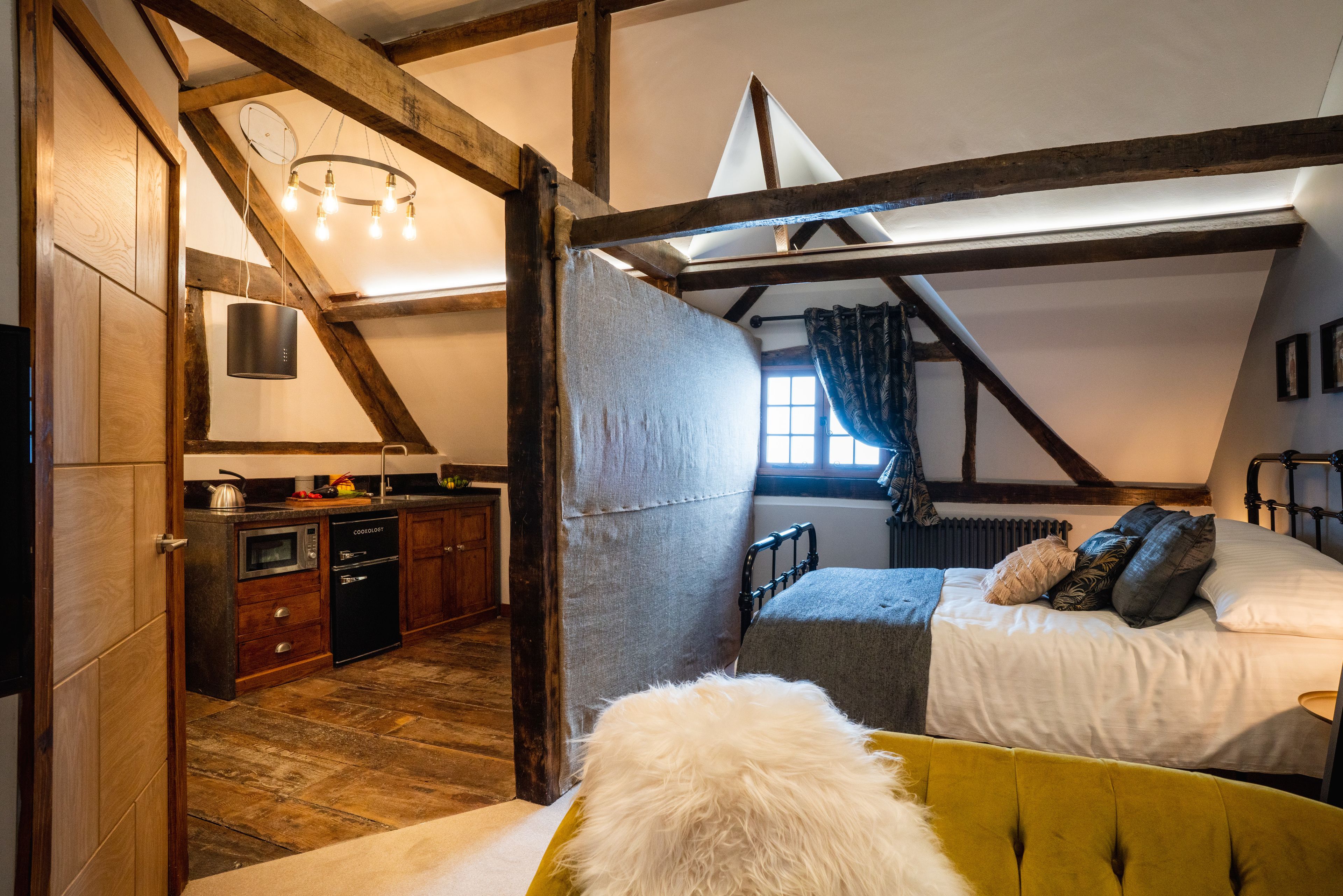 A bedroom with a bed, a window, a radiator, and a kitchen area with cabinets and appliances.