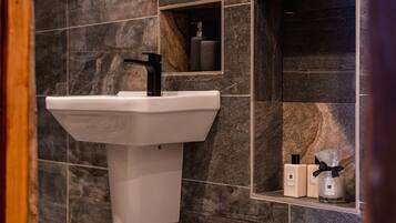 Un baño con un lavamanos de pedestal blanco, un espejo y dos botellas de artículos de aseo en un estante.