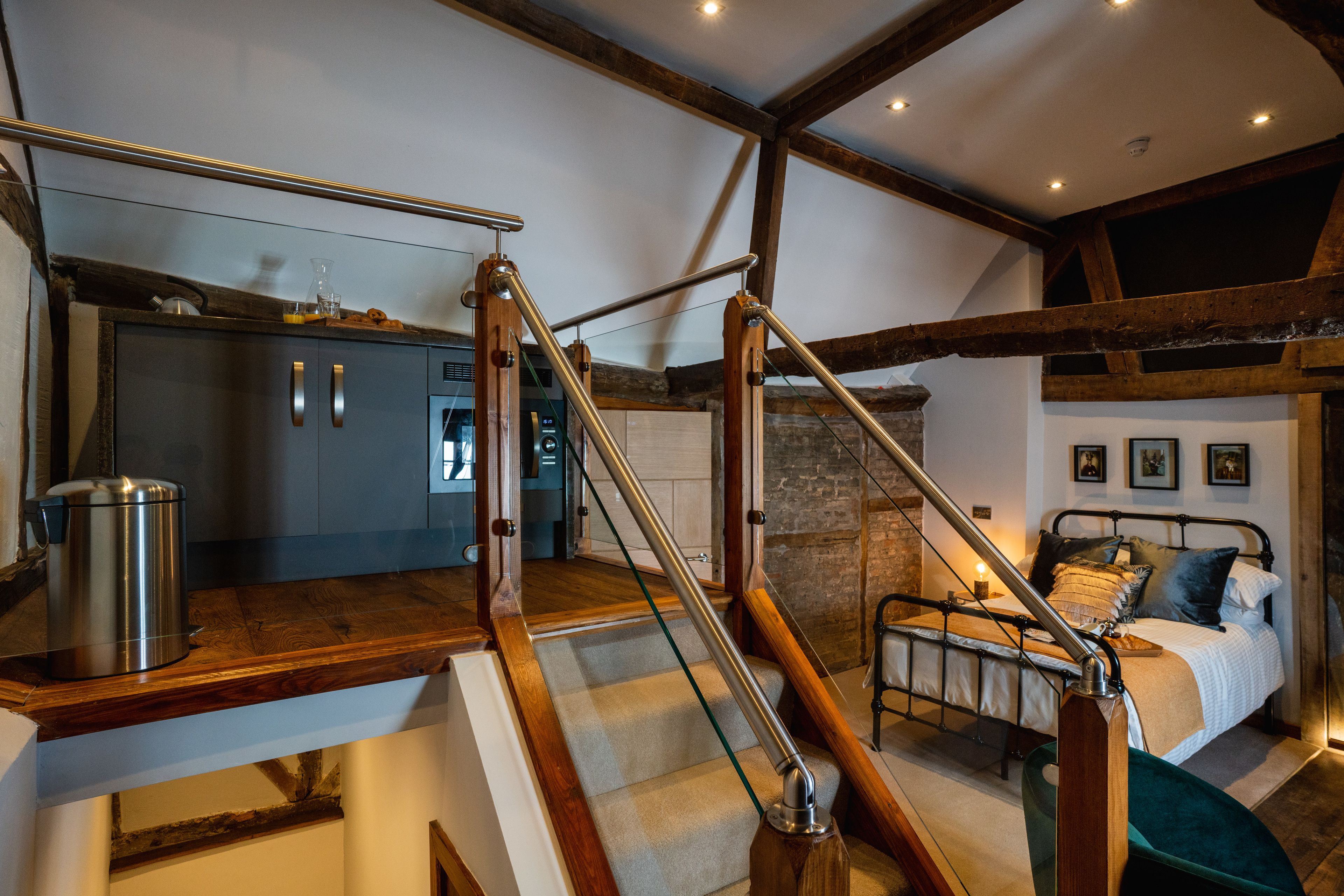 Un dormitorio con una cama, una mesita de noche y una escalera de madera que da a una zona de cocina.