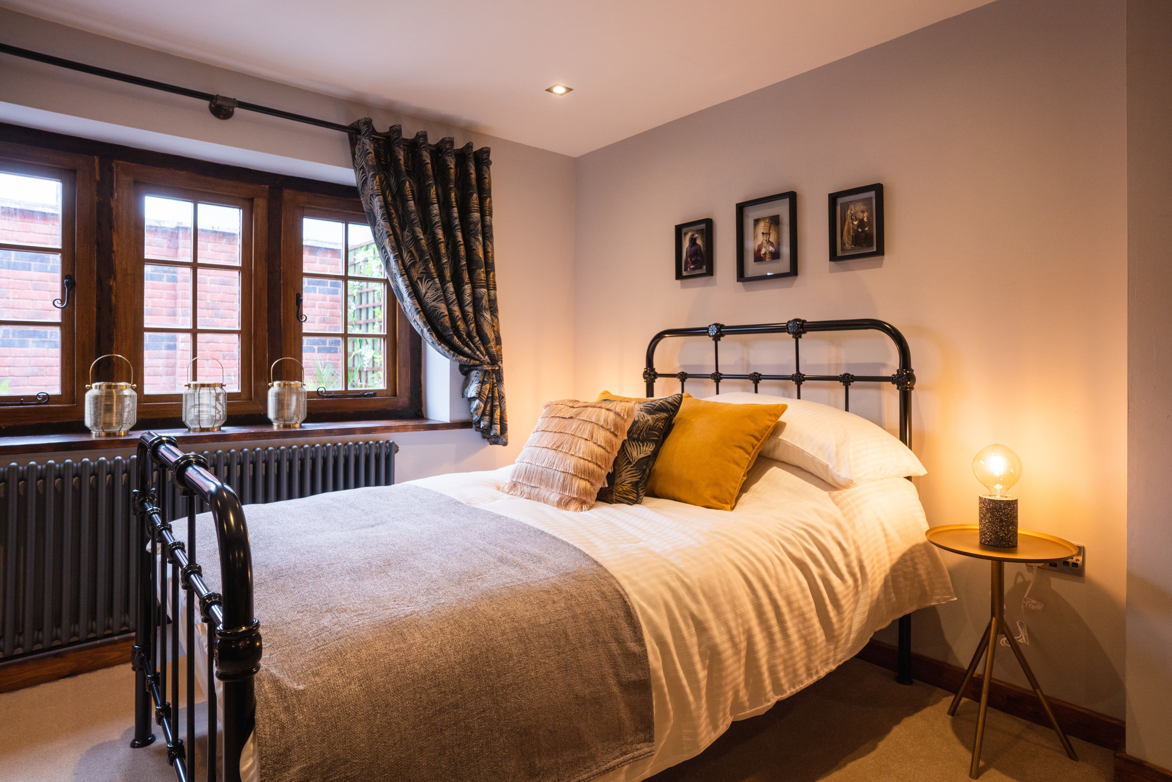 A bedroom with a bed, a radiator, a window with curtains, and a bedside table with a lamp.