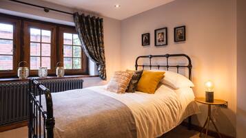 A bedroom with a bed, a radiator, a window with curtains, and a bedside table with a lamp.