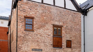 A brick building with a sign reading "Old Infirmary." It has a traditional design with a gabled roof and wooden shutters on the windows. There is a table and chairs outside the building.