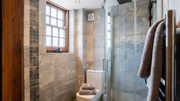 A modern bathroom with a glass shower enclosure, a toilet, and a window.