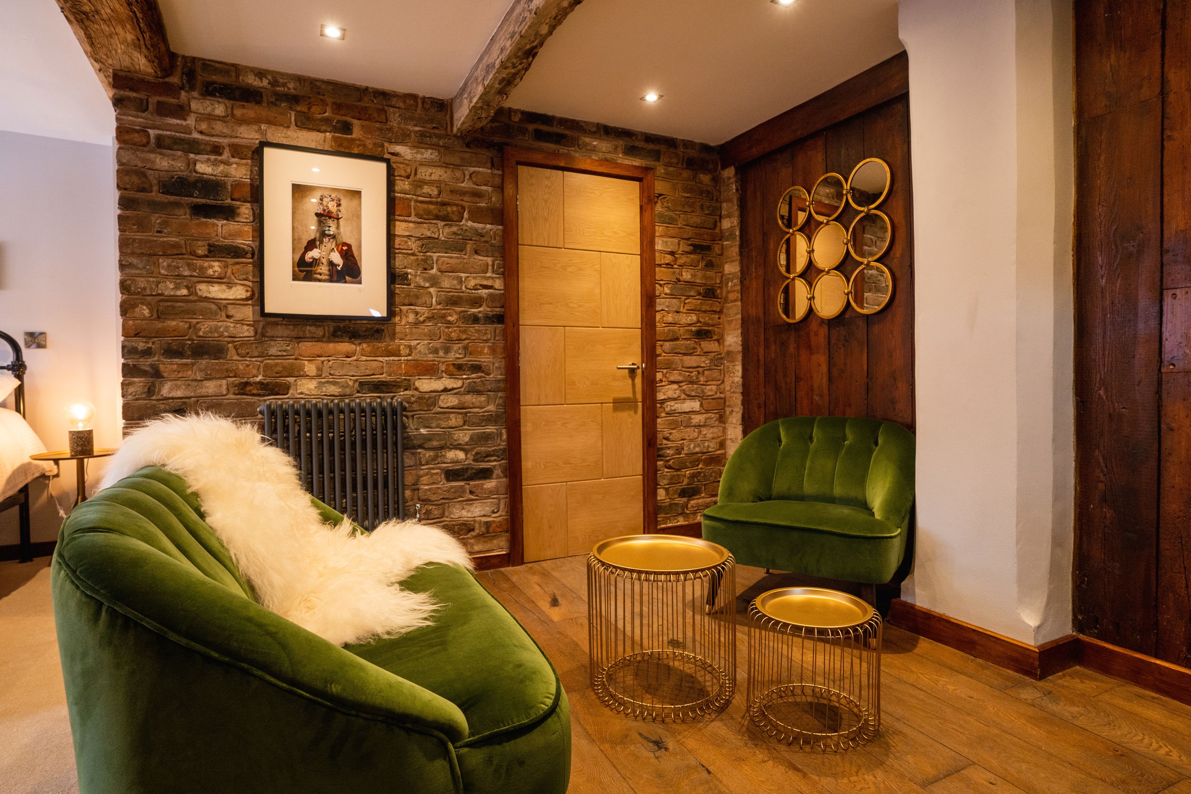 A room with a stone wall, a wooden door, a framed picture, a green chair, and two gold-framed side tables.