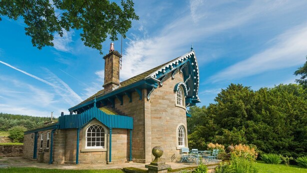 A stone building with a blue roof and a chimney, surrounded by lush greenery. - Swiss Cottage Chatsworth Estate (Chatsworth)