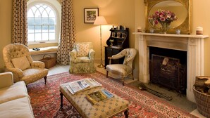 A traditional living room with a fireplace, patterned rug, and classic furniture. - Swiss Cottage Chatsworth Estate (Chatsworth)