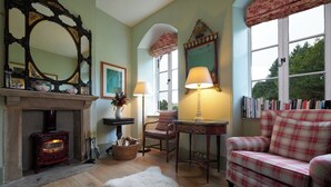 A cozy living room with a fireplace, a sofa, a table with lamps, and a bookshelf. - Russian Cottage Chatsworth Estate (Edensor)